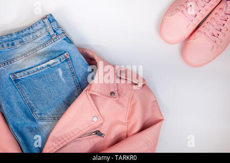 Flat composition with a set of clothes in pink colors. Top view of clothes on a white background. Pink leather jacket, pink sneakers, jeans. Stock Photo
