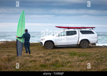 surfer with a big wave surfboard  in front of an all terrain vehicle with another surfboard on top Stock Photo
