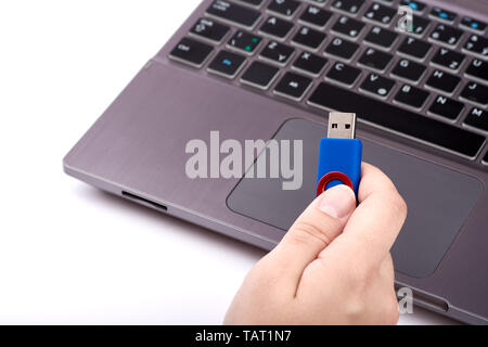 A woman holds a blue USB flash drive in her hand. Silver laptop with black keyboard on blurred background - Isolated on white background. Stock Photo