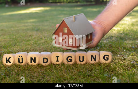 Cubes form the German word 'Kuendigung' ('dismissal' in English) in front of a model house. Stock Photo