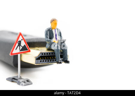 Macro shot on miniature figure as business man working on the laptop notebook sitting on HDMI plug, isolated on white background. Information technolo Stock Photo