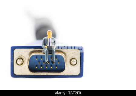 Macro shot on miniature figure as business man working on the laptop notebook sitting on video VGA plug, isolated on white background. Information tec Stock Photo