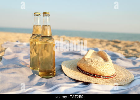 Closeup of two beer glass bottles on sandy tropical beach towel near straw hat. Blue ocean lagoon on background. Refreshing beverage on hot summer day Stock Photo