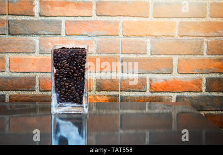 Roasted coffee beans in glass on table with old brick wall background Stock Photo
