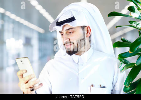 Arabian (Gulf area) smiling man with traditional wear and using a mobile phone. Stock Photo