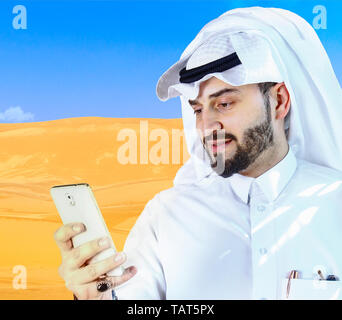 Arabian man using a cellphone on desert background. Stock Photo