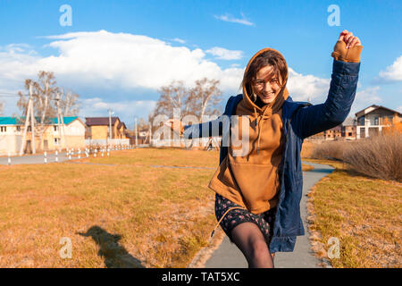 A beautiful woman in a warm sweatshirt, dress, jacket and sneakers walks, has fun, behaves funny, rests, enjoys nature on a warm summer day Stock Photo