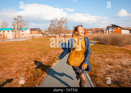 A beautiful woman in a warm sweatshirt, dress, jacket and sneakers walks, has fun, behaves funny, rests, enjoys nature on a warm summer day Stock Photo