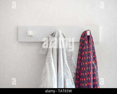 White relaxed striped shirt and red polka dot pattern scarf hanging on white modern hanger on white wall background. Stock Photo