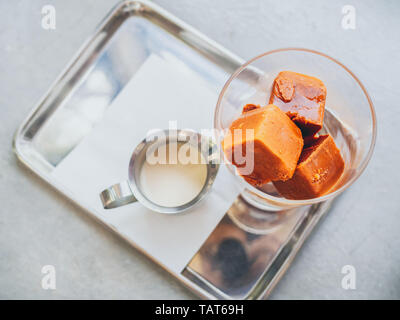Thai milk tea ice cubes in glass with milk in small jug on stainless steel tray on concrete table top view. Stock Photo