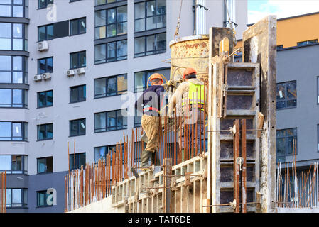 Workers poured concrete in the formwork of the walls on the construction of the house against the background of a modern residential building. Stock Photo