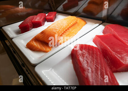 Three large pieces of tuna and salmon for sushi lie on a white plate in the refrigerated counter. Stock Photo