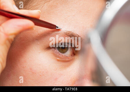Close up picture of young woman holding a stainless steel eyebrow clipper, doing her eyebrows Stock Photo