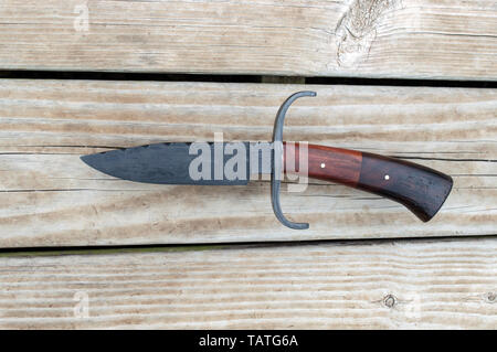 This hand forged Damascus bowie knife is a rather unique collectors item. Displayed on a contrasting wooden deck. Stock Photo