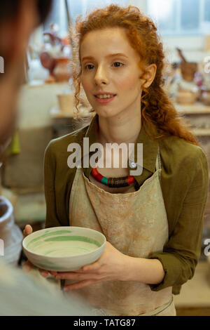 Painted clay plate. Smiling long-haired girl presenting hand-made clay plate to her teacher during masterclass in pottery Stock Photo