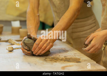 Couple having masterclass. Strong man tightly pressing piece of fresh clay on a wooden table while student staying nearby Stock Photo