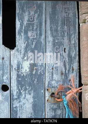 Ancient blue-stained barn door with old carved graffiti, woodworm, grain & rusty nails fastened with blue & orange baler twine tied to rusty door ring Stock Photo