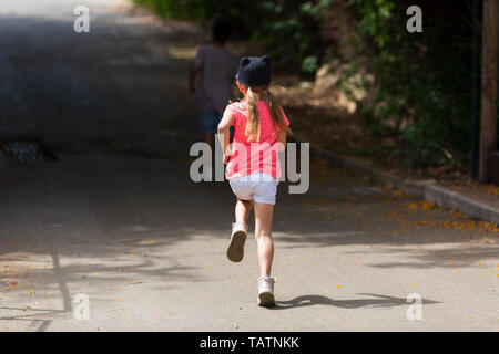 Children run on park walkway into arch made of green plants, rear view Stock Photo