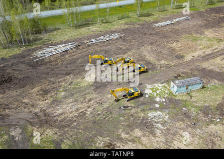 Aerial side view of four yellow crawler excavators standing on ground near the construction site and waiting for the working day to start digging the  Stock Photo