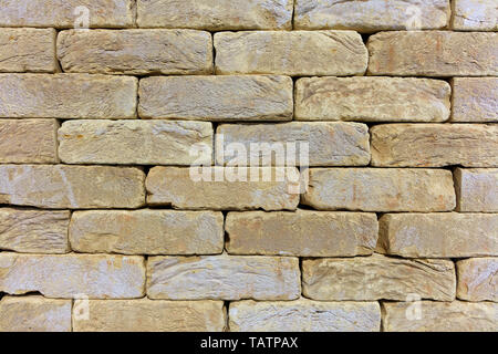 Texture and background of the wall of the old stone from beige-golden sandstone in the form of a brickwork. Stock Photo