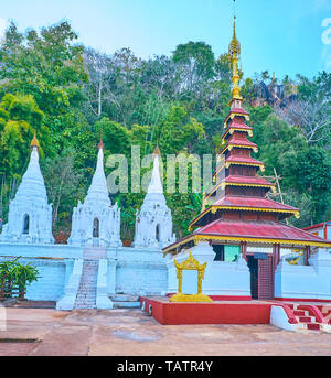 The white pagodas and old shrine with tall wooden pyatthat (multistaged) roof in historic Buddhist monastery, located next to Shwe Oo Min cave complex Stock Photo