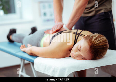 So relaxing. Nice middle aged woman lying on the medical bed while enjoying her back massage Stock Photo