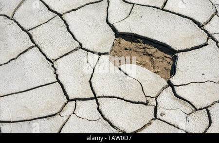 Very dry layer of soil with cracks formed due to a lack of water and one piece peeled away revealing the ground beneath. Stock Photo