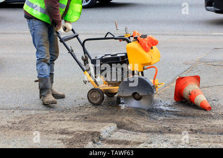 An employee of the road maintenance service removes old asphalt with a gasoline carver during repairs on the carriageway. Stock Photo