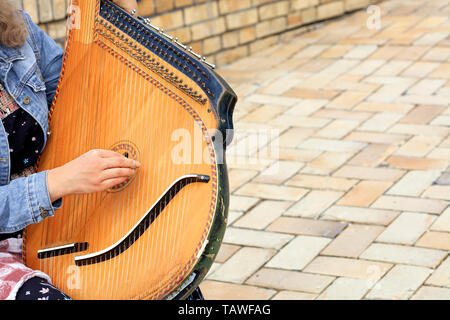 The musician plays the old Ukrainian ethnic musical instrument bandura (pandora) against the background of the old cobblestone road. Stock Photo