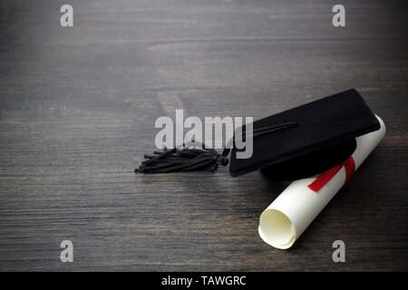 Black Graduation Cap with Degree on dark Wooden Background. Stock Photo