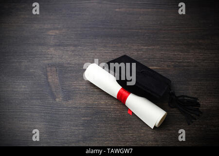 Black Graduation Cap with Degree on dark Wooden Background. Stock Photo