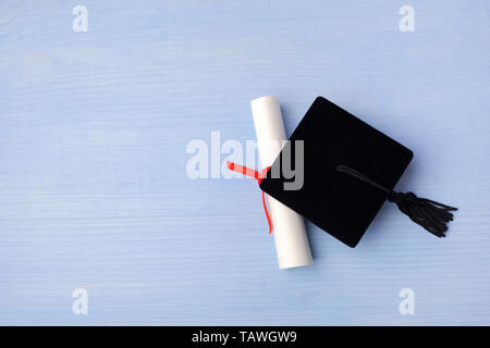 Black Graduation Cap with Degree on light blue Wooden Background. Stock Photo