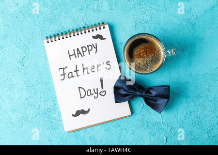 Notebook with inscription happy fathers day, blue bow tie and cup of coffee on color background, space for text and top view Stock Photo