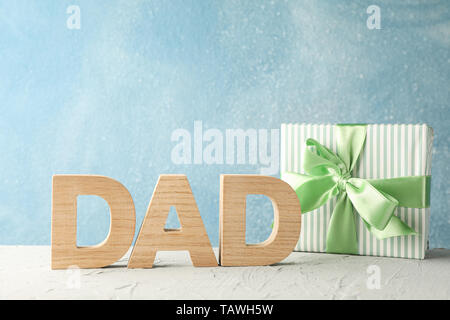 Gift box with green ribbon and inscription DAD on white table against blue background, space for text Stock Photo