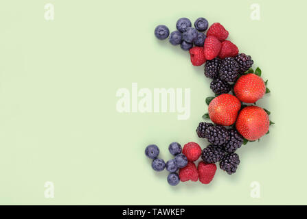 Summer Berries arranged in a half circle on plain green background with plenty of copy space Stock Photo