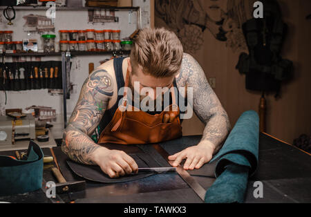 Leather Currier wording with leather goods at a workshop. Stock Photo