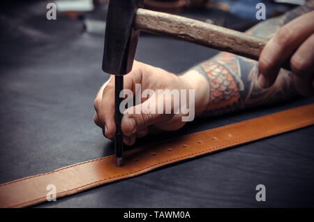 Leather workman manufacturing new leather product in leather shop. Stock Photo