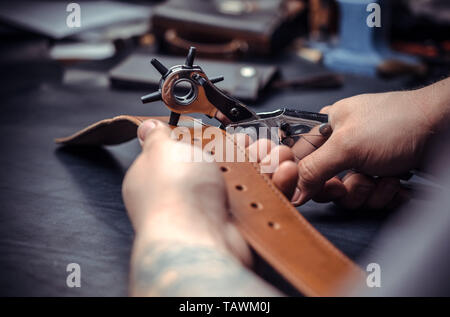Currier cutting out leather goods in his workshop. Stock Photo