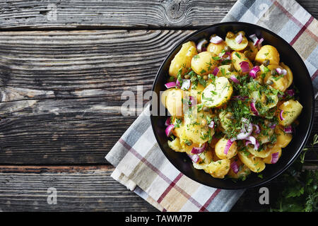 delicious new potato salad with red onion, capers, greens in a black bowl, horizontal view from above, copy space Stock Photo