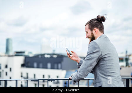 A young businessman with smartphone standing on a terrace, text messaging. Stock Photo