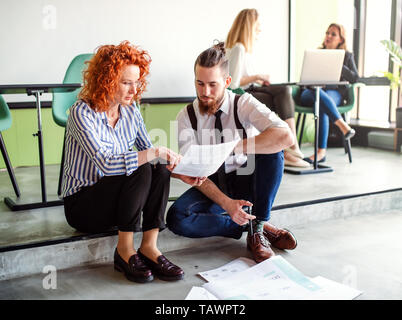 Two business people looking at paper documents in an office, talking. Stock Photo