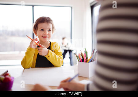 A small girl with unrecognizable mother drawing in a kitchen. Stock Photo