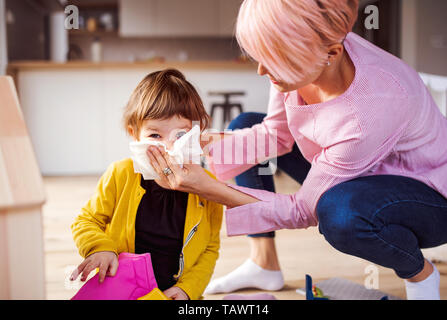 Mother blowing her small daughter's nose when playing at home. Stock Photo