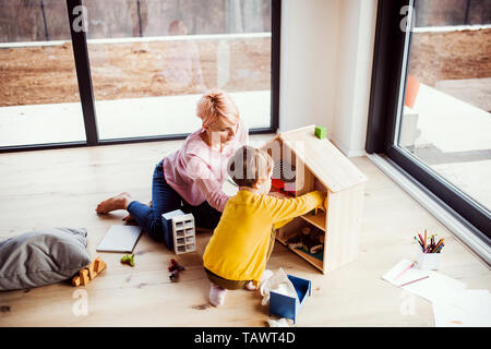 A young woman and small daughter playing with wooden house on the floor. Stock Photo