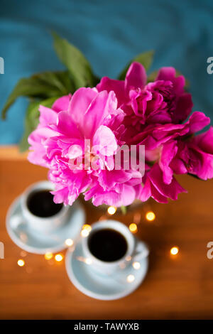 Coffee and pink peonies on a wooden tray in bed with bright bedding. Close-up Stock Photo