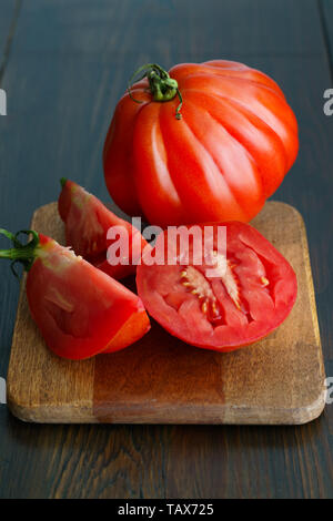 Large freshly harvested whole and sliced oxheart tomatoes. Dark wooden table, high resolution Stock Photo