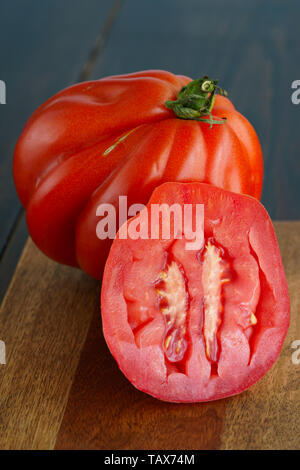 Large freshly harvested whole and sliced oxheart tomatoes. Dark wooden table, high resolution Stock Photo