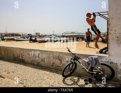 24.02.2019, Sal Rei, Boa Vista, Cape Verde Islands - Local men workout in the open air Gym, fishing boats at the beach Praia de Diante. 00X190224D124C Stock Photo
