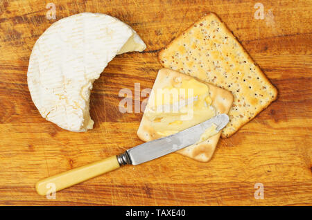 Camembert cheese with biscuits and a knife on a wooden chopping board, top view Stock Photo