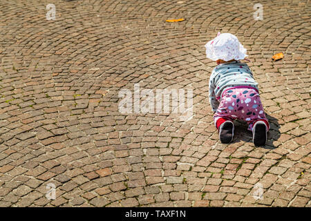 back of cute funny baby wearing white hat and pink pants crawling on cobbledstones on Italy Stock Photo